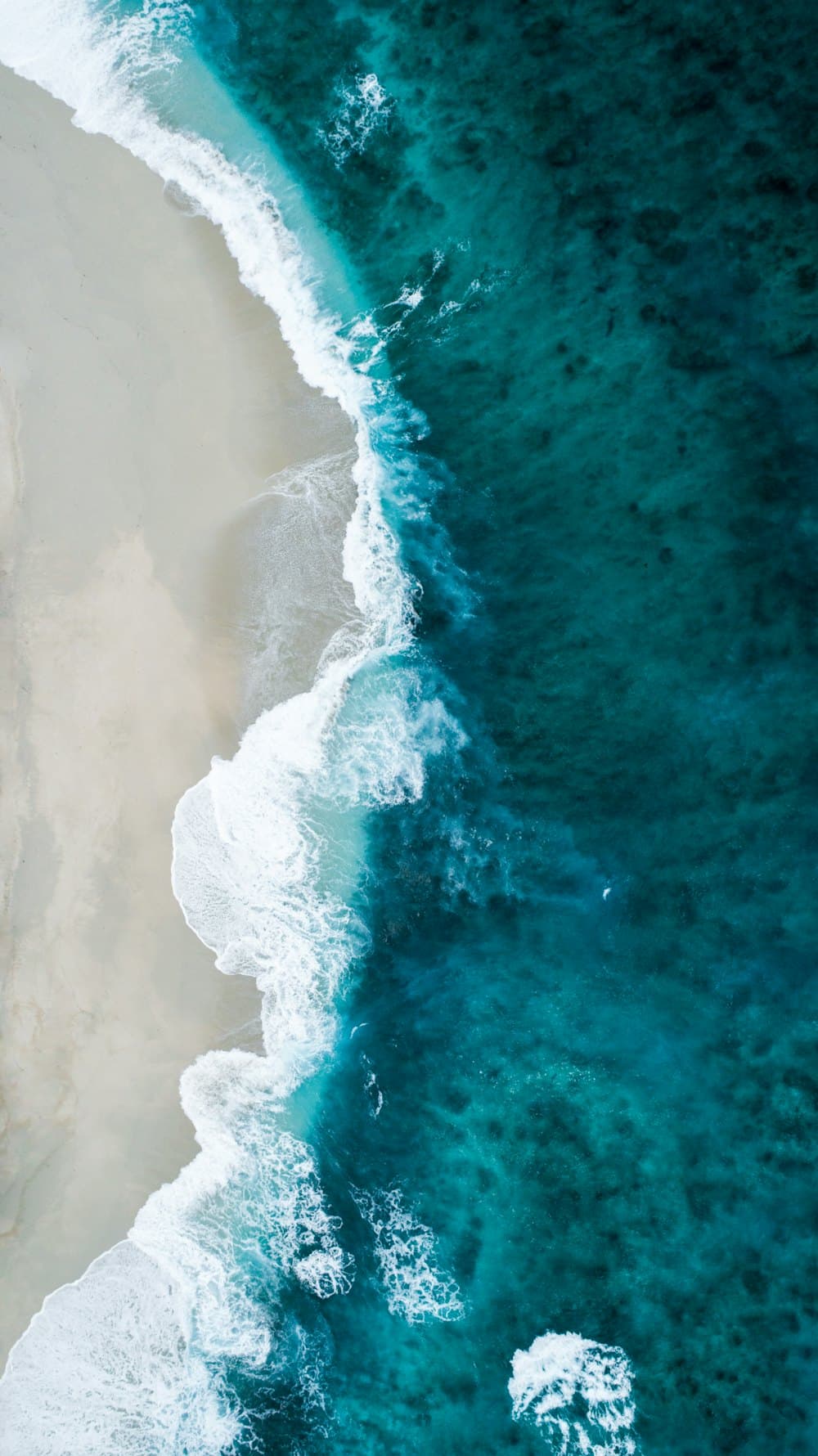 Turquoise water meeting pale sand, seen from above.